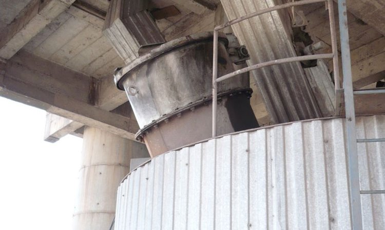 An awkwardly designed and installed explosion vent on a pulverised coal silo. The silo has been installed in a building, which disallows explosion venting without special measures that control the blast’s exit from the building. These are not present. The explosion vent is of a design that will not reclose, due to design faults that will cause its hinged lid to deform and not to fall back after the explosion, leaving it open to ingress of O2 and uncontrolled losses of inerting medium that will make firefighting impossible. Explosion pressure shock resistance of the silo and the explosion vent are lacking. The explosion effects will affect the silo’s in-feed drop chutes. When venting, the blast will hit the concrete ceiling, which is far too close to prevent the flame body’s dangerous deflection, spread and expansion into the building.